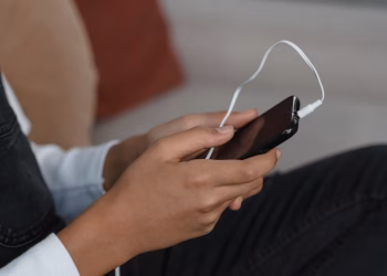 A person holds a smartphone with earbuds connected, capturing modern technology engagement.