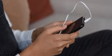 A person holds a smartphone with earbuds connected, capturing modern technology engagement.