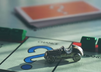 A close-up of a Monopoly board game featuring a silver car token and chance card.