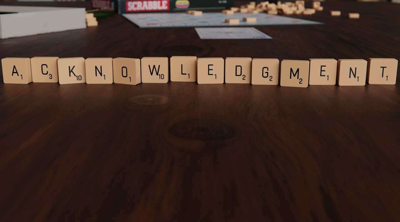 Scrabble tiles spelling out acknowledgement on a wooden surface.
