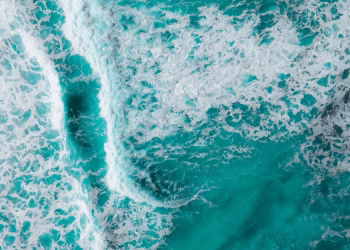 Captivating aerial shot of vibrant turquoise ocean waves crashing with foamy textures.
