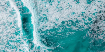 Captivating aerial shot of vibrant turquoise ocean waves crashing with foamy textures.