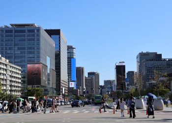 Vibrant street scene in Seoul with skyscrapers and people crossing under a clear blue sky.