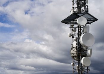 A telecommunication tower equipped with satellite dishes against a cloudy sky.