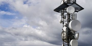 A telecommunication tower equipped with satellite dishes against a cloudy sky.