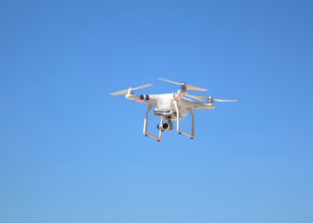 A white drone captured mid-flight against a clear blue sky, showing technology in motion.