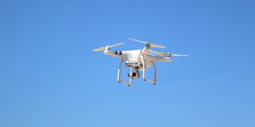 A white drone captured mid-flight against a clear blue sky, showing technology in motion.