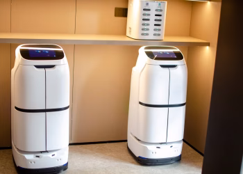 Two white robotic delivery systems located in a modern indoor room with soft lighting.