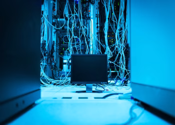 A complex network of cables in a data center with a monitor in the foreground.