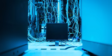 A complex network of cables in a data center with a monitor in the foreground.