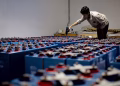 A worker checking many industrial batteries inside a facility. Indoor, industrial setting.