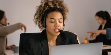 Customer support agent with headset working on laptop in office.
