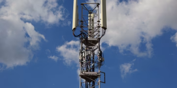 A tall cellular communication tower against a vivid blue sky, symbolizing modern technology.