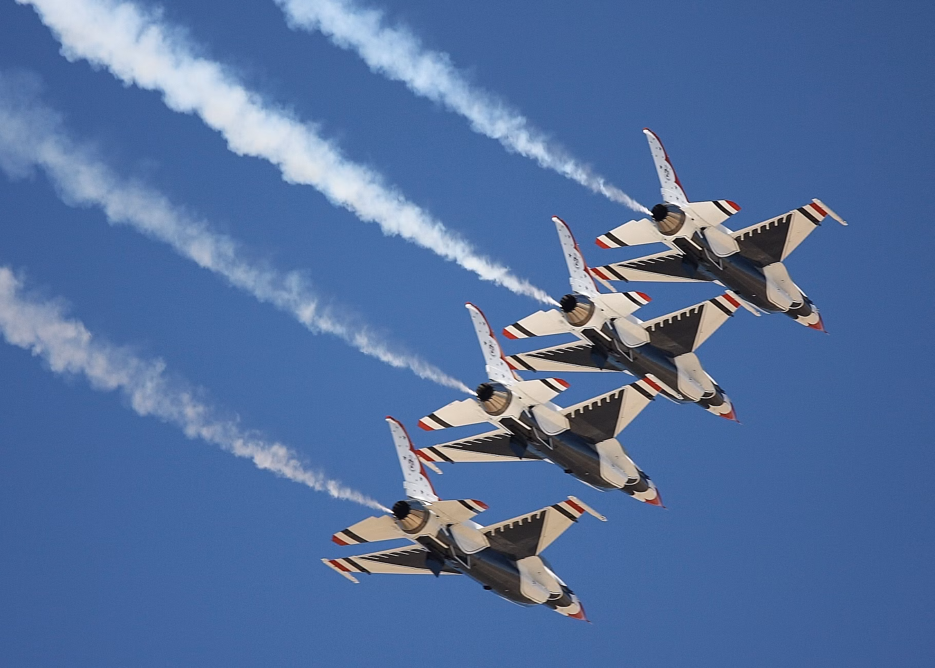 Four fighter jets performing a precise aerial formation with vapor trails against a clear blue sky.