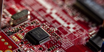 Detailed macro shot of a red circuit board, highlighting electronic components and microchips.