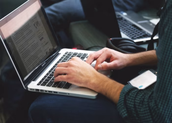 A programmer typing on a laptop in an indoor setting, showcasing technology in use.