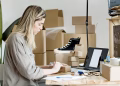A woman packing boxes for her online store, surrounded by packaging materials and a laptop.