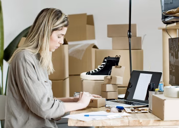 A woman packing boxes for her online store, surrounded by packaging materials and a laptop.