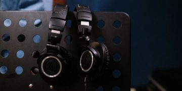 Close-up of professional headphones hanging on a perforated music stand in a studio setting.