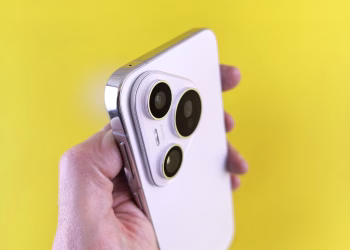 A close-up shot of a modern smartphone camera lens held against a bright yellow backdrop.