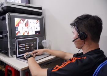 Technician manages multiple video feeds using laptop and monitor in studio setting.