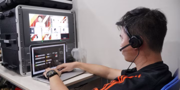 Technician manages multiple video feeds using laptop and monitor in studio setting.