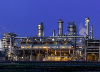 A striking view of an industrial facility in Zuid-Holland, illuminated at dusk against a clear blue sky.