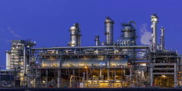 A striking view of an industrial facility in Zuid-Holland, illuminated at dusk against a clear blue sky.