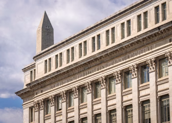 US Department of Agriculture building with Washington Monument behind, blue sky with clouds.