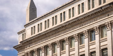 US Department of Agriculture building with Washington Monument behind, blue sky with clouds.