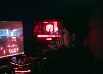 Man playing a video game on a desktop with glowing red and blue lights.