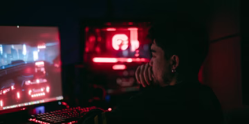 Man playing a video game on a desktop with glowing red and blue lights.
