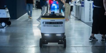 Autonomous delivery robot navigating indoors during a technology event.