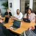 four people all on laptops, two men and two women, listen to person talking in a board meeting