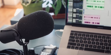 A podcast recording setup with a laptop, microphone, and audio equipment indoors.