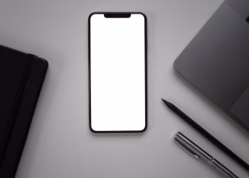 Flat lay of a sleek desk featuring a smartphone mockup beside a laptop, pen, and notebook.