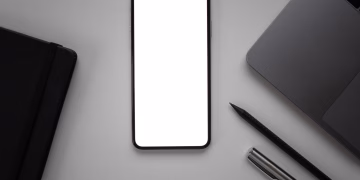 Flat lay of a sleek desk featuring a smartphone mockup beside a laptop, pen, and notebook.