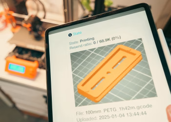 Close-up of a digital tablet displaying a 3D printing process in a workshop setting.