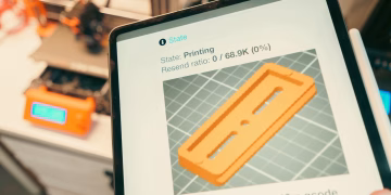 Close-up of a digital tablet displaying a 3D printing process in a workshop setting.