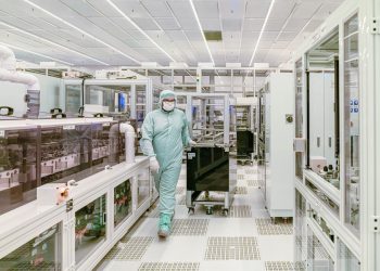 Scientist in protective gear walking in a high-tech cleanroom laboratory environment.