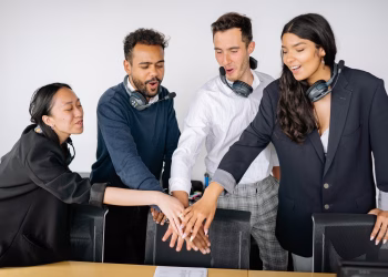 A diverse group of colleagues in an office setting putting their hands together to symbolize teamwork.