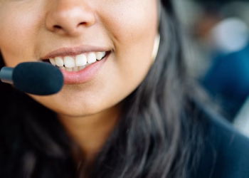 Close-up of a smiling customer service agent wearing a headset in an office environment.