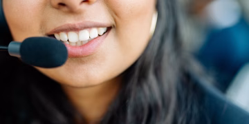 Close-up of a smiling customer service agent wearing a headset in an office environment.