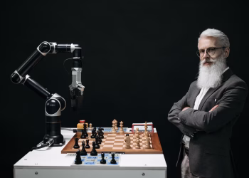 A robotic arm and a bearded man engaged in a strategic chess game highlighting technology and innovation.