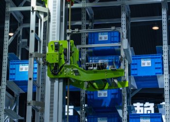 High-tech automated warehouse system featuring a green robotic arm handling blue storage crates.