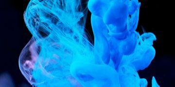 Dynamic blue ink swirls in water creating abstract shapes on a dark backdrop.