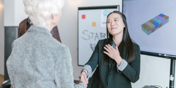 Professional women shaking hands in a corporate office setting, symbolizing a successful business agreement.
