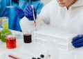 Female scientist in lab coat using pipette on test tubes, focusing on colorful chemical analysis.