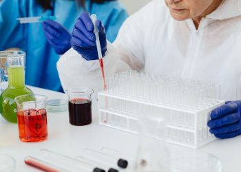 Female scientist in lab coat using pipette on test tubes, focusing on colorful chemical analysis.