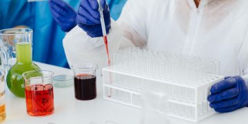 Female scientist in lab coat using pipette on test tubes, focusing on colorful chemical analysis.